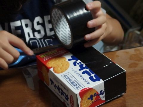 黒い布粘着テープをお菓子の空き箱とポテトチップスの筒に貼って、カメラのように組み立てて貼り合わせます。